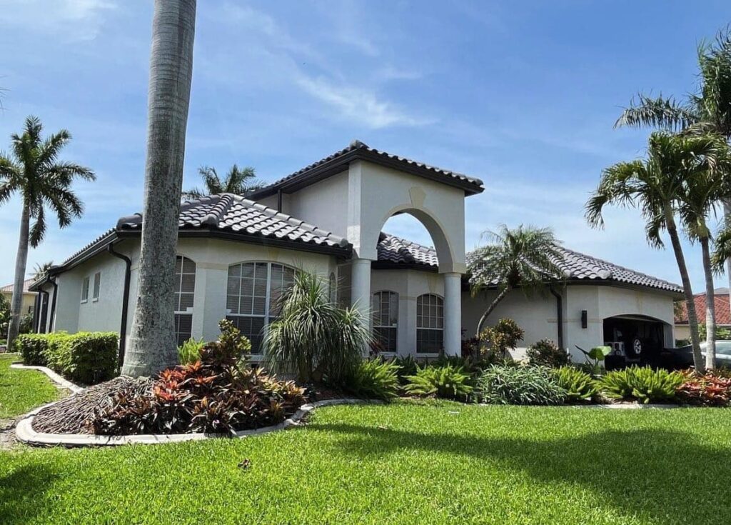 a house surrounded by plants, grass, and a palm tree