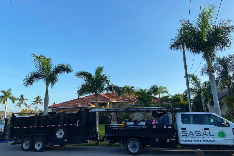 A truck and trailer from Sabal Construction and Roofing parked in front of a house.