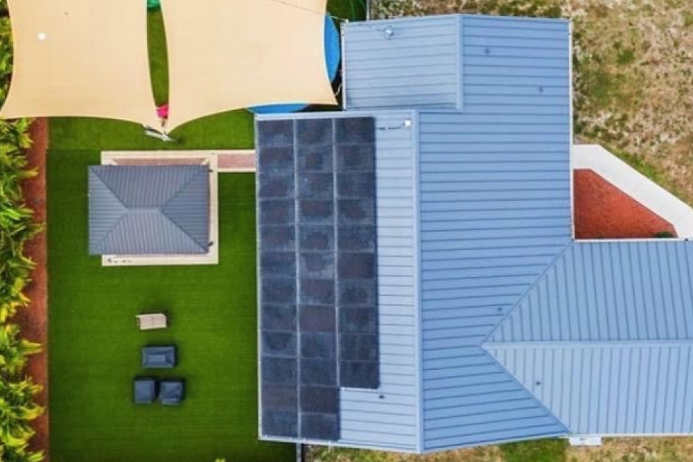 A residential backyard showcasing a blue-roofed house equipped with solar panels