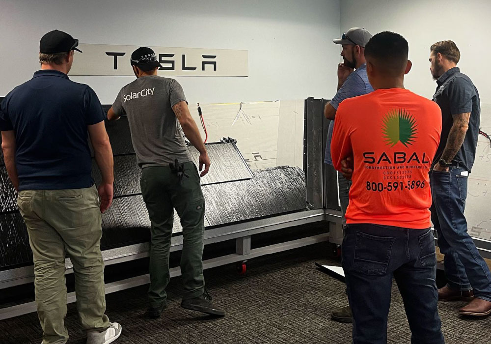 A group of five people standing in front of a Tesla solar panel display.