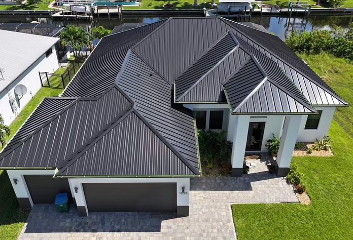 Modern house with a sleek black metal roof, white exterior, and a canal view.